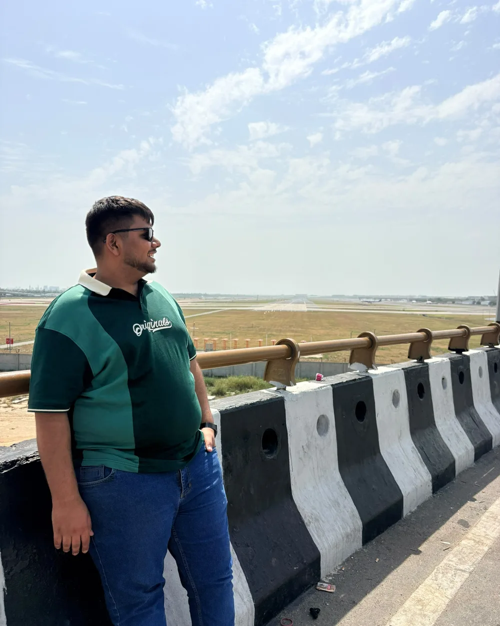 Prakarsh leaning on a flyover railing beside an airport runway